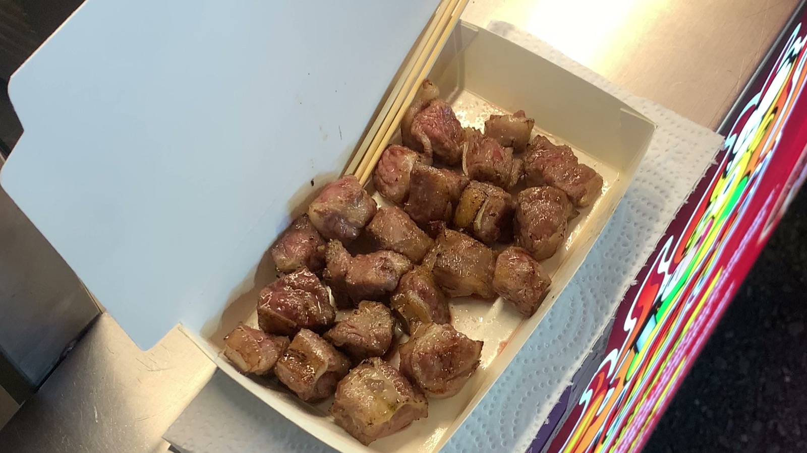 A paper boat of grilled beef cubes (骰子牛) with a bamboo skewer, at a Taiwanese street food stand